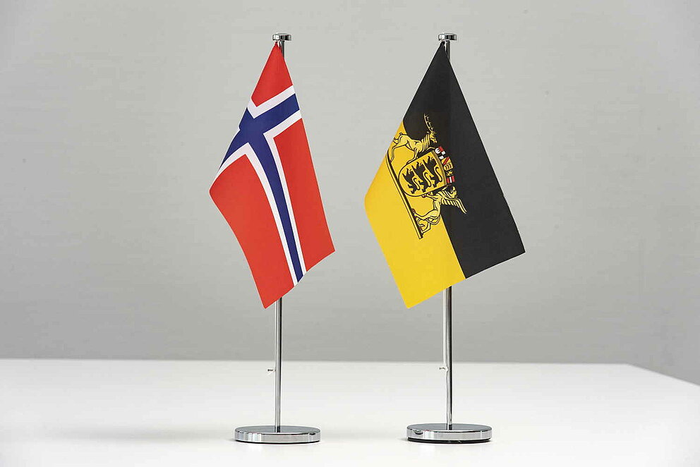 Flaggen von Norwegen und Baden-Württemberg stehen als Wimpel auf einem Tisch.