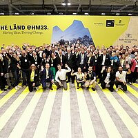 Ministerpräsident Winfried Kretschmann und 44 Mitaussteller posieren für ein Gruppenfoto am THE LÄND Pavillon, um die Vielfalt und Stärke der Region zu zeigen.