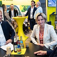Eine Frau und ein Mann sitzen an einem Tisch und unterhalten sich mit zwei weiteren Personen.