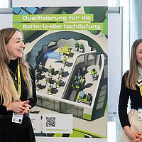 Marleen Keller und Lena Müller vor einem QualiBatt BW Poster. Sie lachen.