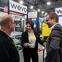 Drei Menschen unterhalten sich auf einer Messe miteinander.