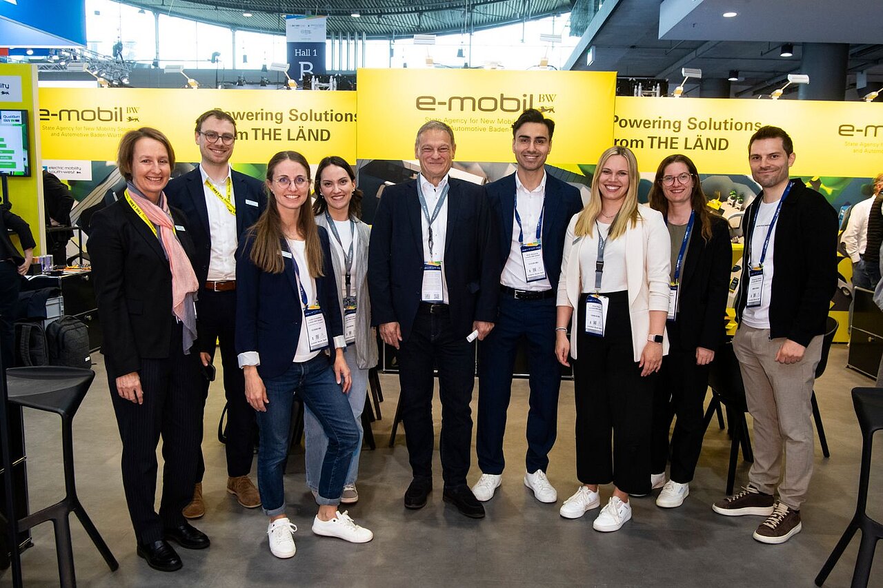 Eine Gruppe Menschen steht auf dem Messestand und lächelt in die Kamera.