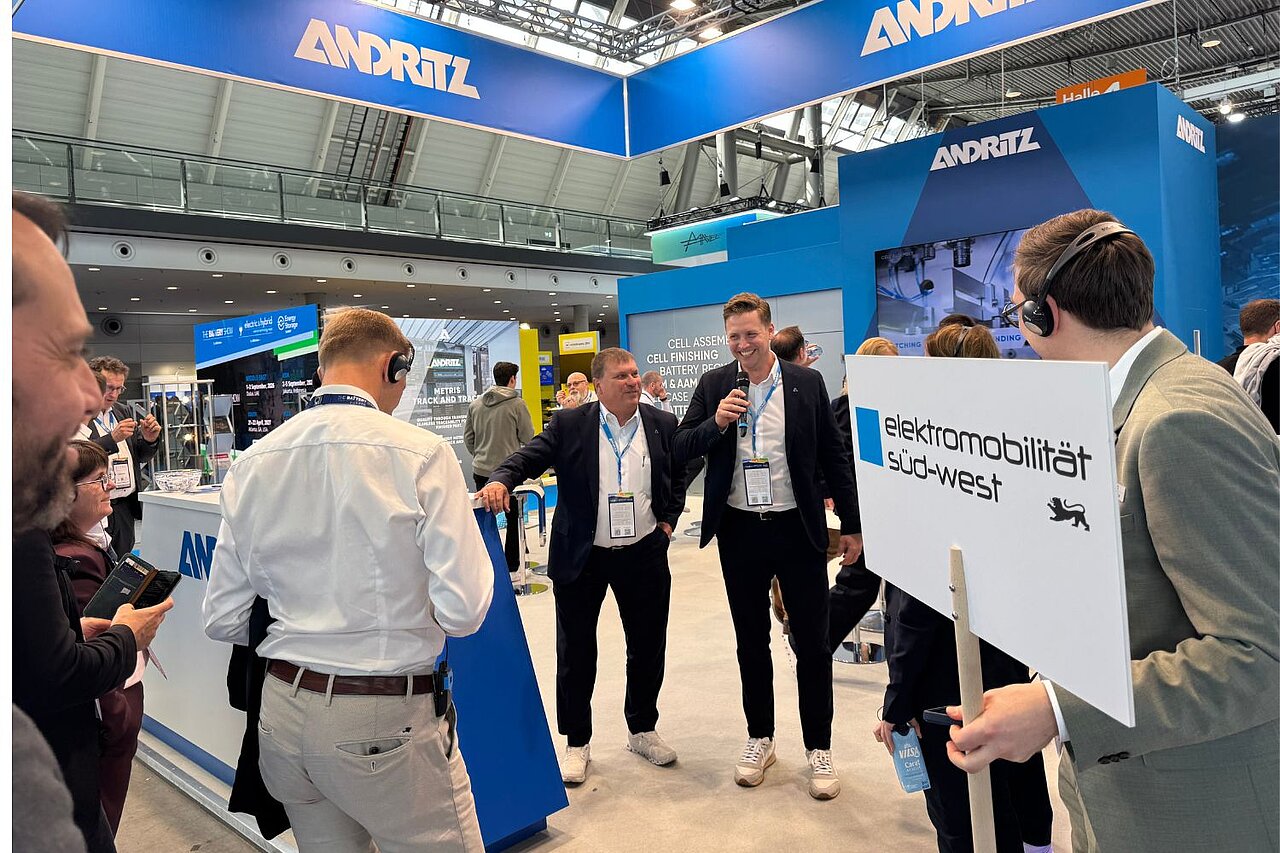 Eine Personengruppe steht auf dem Messestand von Andritz Schuler Pressen und hört zwei Personen zu, die einen Vortrag halten.