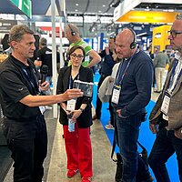 Drei Männer und zwei Frauen unterhalten sich auf einem Messestand. 