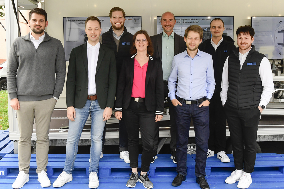 Acht Personen stehen in zwei Reihen und blicken lächelnd in die Kamera.