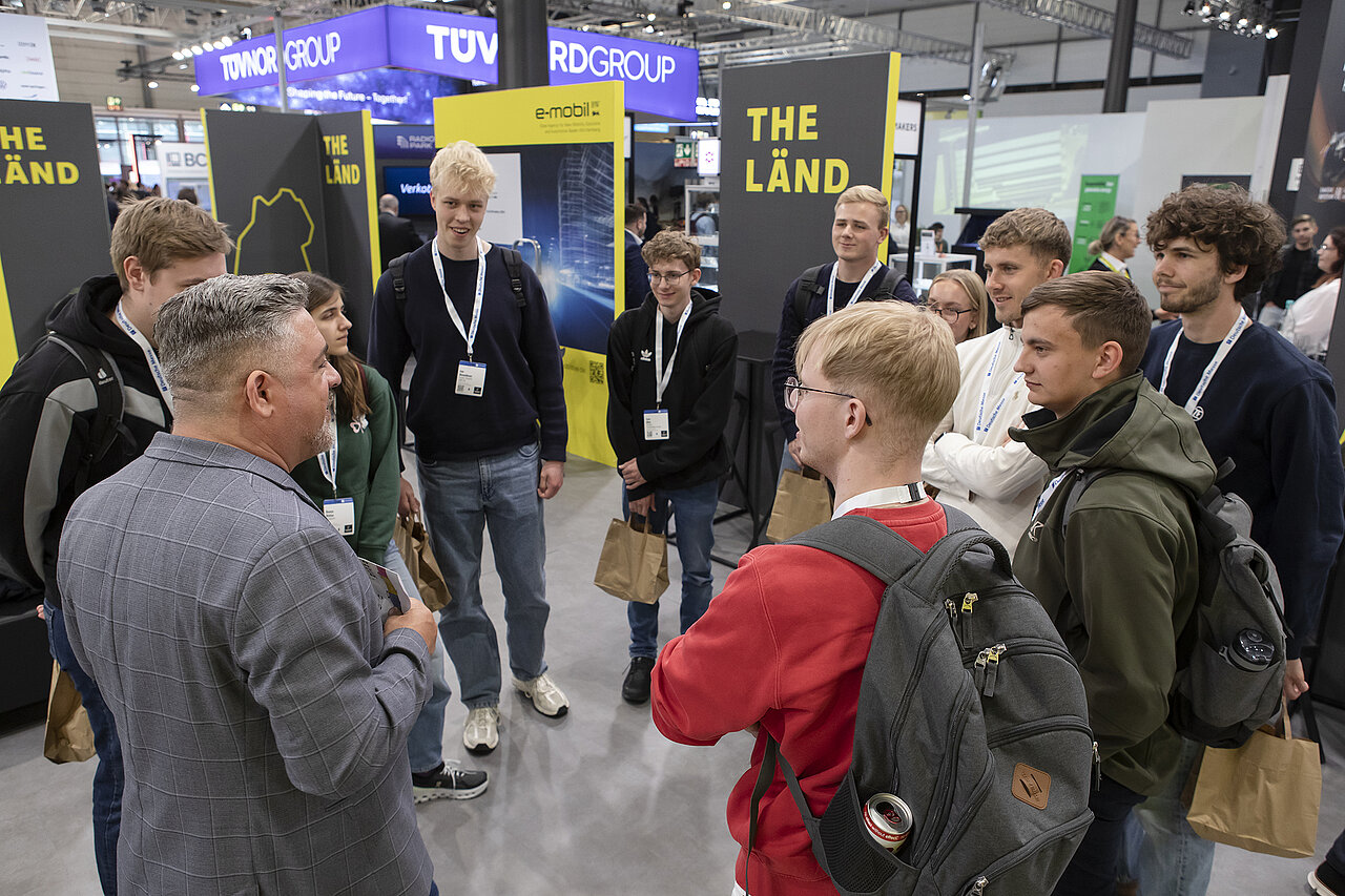 Eine Gruppe Besuchern steht im Kreis zusammen auf einem Messestand.