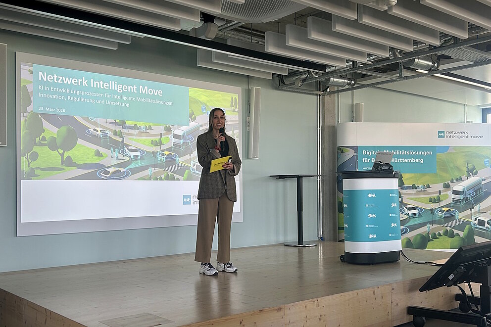 Das Bild zeigt eine Mitarbeiterin der e-mobil BW GmbH beim Moderieren einer Veranstaltung. Die Mitarbeiterin hält ein Mikrofon und schaut ins Publikum.
