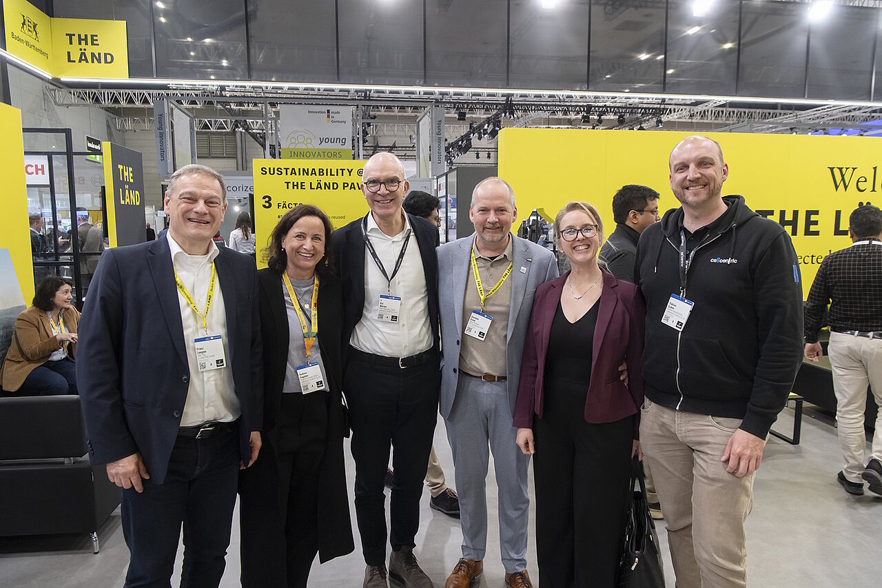 Sechs Personen stehen auf einem Messestand im gelben THE LÄND Design.