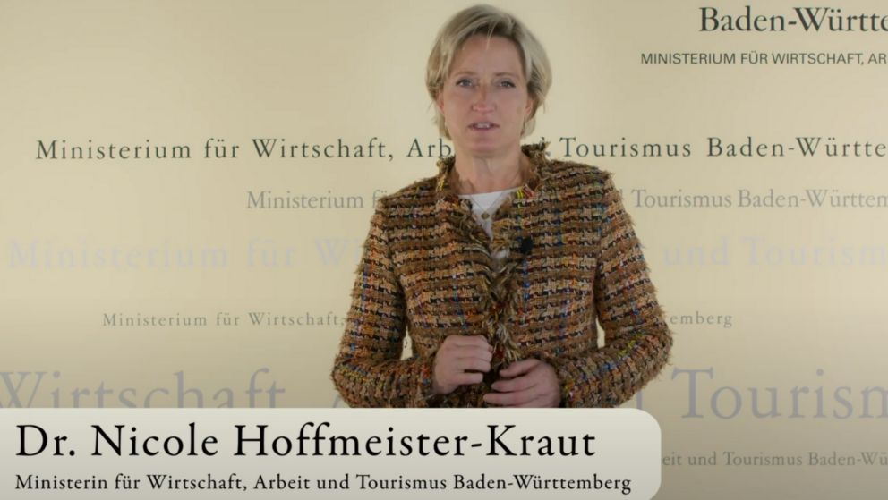 Dr. Nicole Hoffmeister-Kraut steht vor einem gelbem Hintergrund, darauf ist das Logo des Landes Baden-Württemberg zu sehen. Im Vordergrund wird in einer Bauchbinde ihr Name eingeblendet.