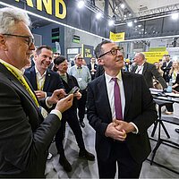 3 Männer, darunter Cem Özdemir, unterhalten sich vor einer Wand.