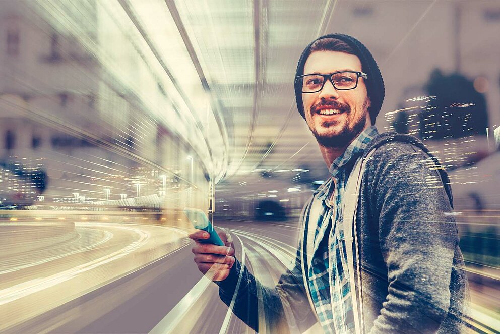 Porträt eines jungen Mannes, der am Handy tippt. Im Hintergrund befindet sich eine Straße mit Skyline.