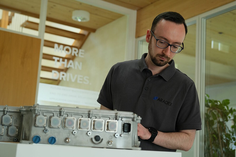 Ein grauer Inverter neben einem Mitarbeiter im schwarzen Tshirt der Firma Aradex.
