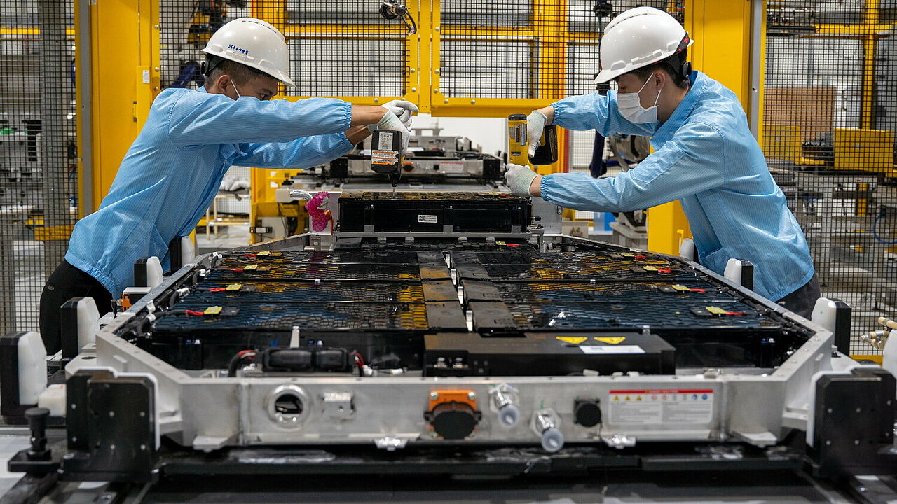 Zwei Menschen arbeiten in einer Fabrik an einer Batterie für Elektrofahrzeuge. 