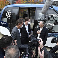 Wirtschaftsvertreter: innen im Gespräch vor einem autonomen Shuttle bei der SDA-Jahresveranstaltung.