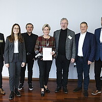 Die baden-württembergische Wirtschaftsministerin Dr. Nicole Hoffmeister-Kraut besucht den Zulieferertag Automobilwirtschaft BW 2022. Es ist ein Gruppenfoto gemeinsam mit den internationalen Gästen zu sehen..