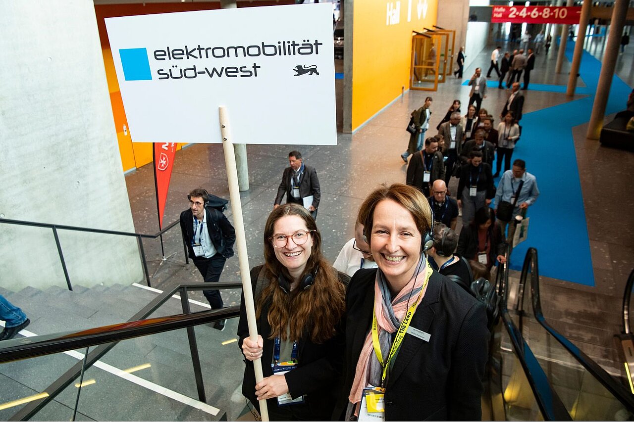 Zwei Frauen halten ein Schild mit dem Titel "Elektromobilität Süd-West".