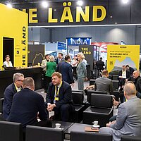 Viele Menschen sitzen auf Sofas während einer Messe und unterhalten sich.