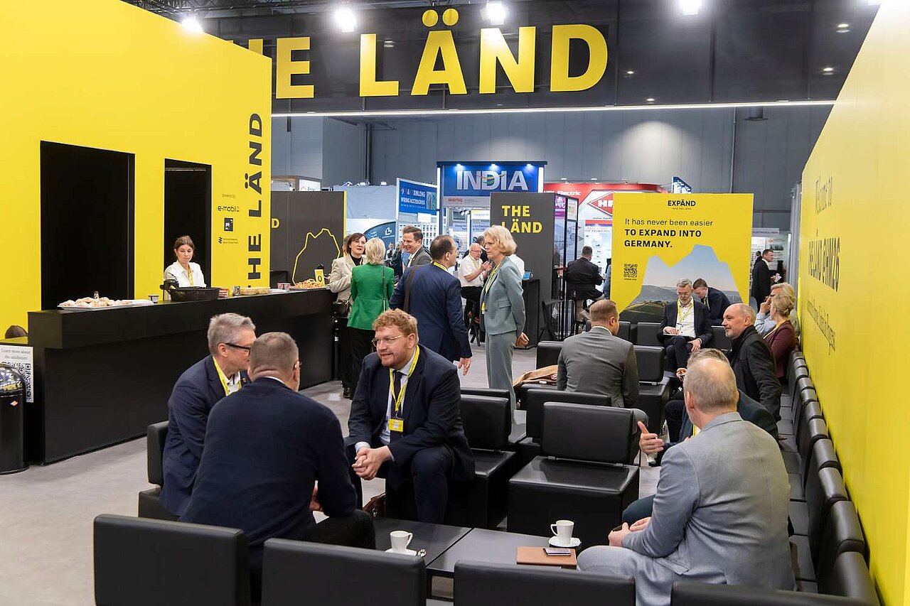 Viele Menschen sitzen auf Sofas während einer Messe und unterhalten sich.