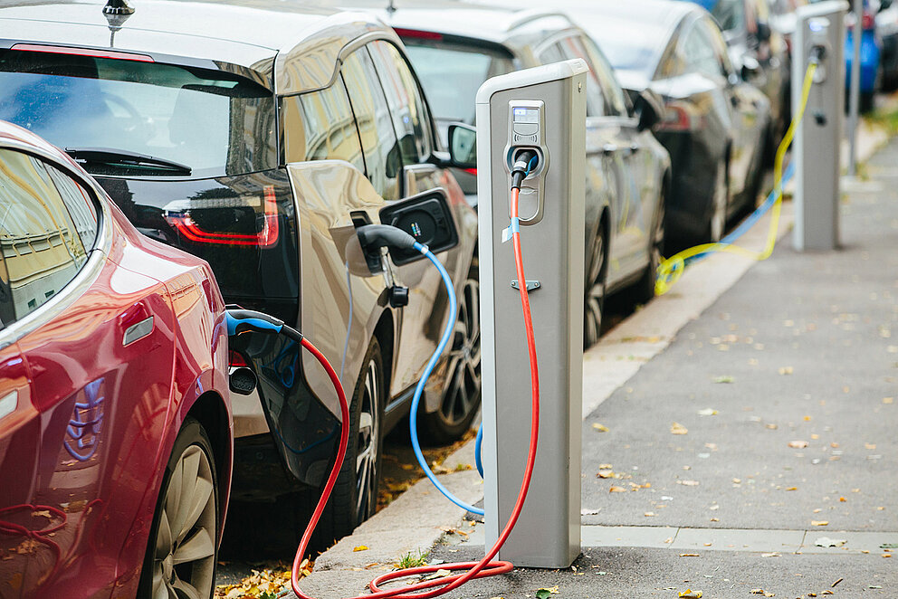 Mehrere elektrische PKW, die geparkt am Straßenrand, an Ladestationen angeschlossen sind