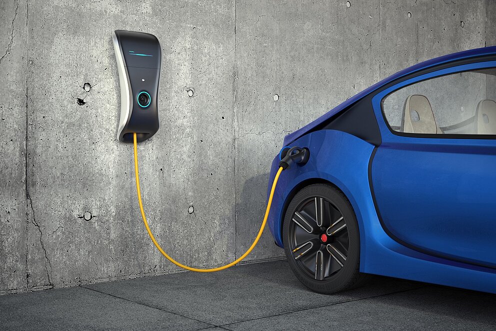 Ein E-Auto lädt an einer Wallbox die an einer Betonwand in einer Tiefgarage hängt.
