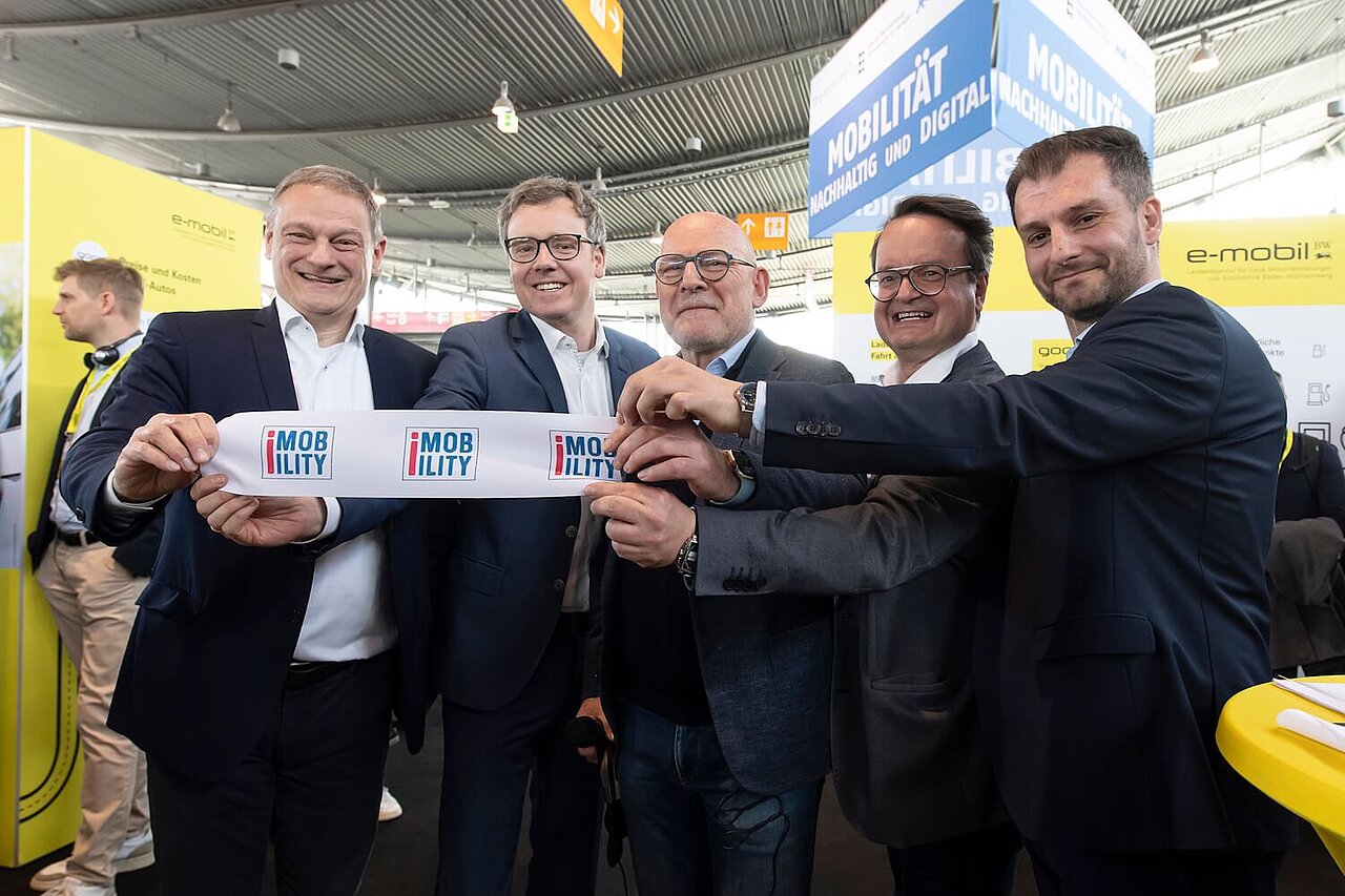 Fünf Personen halten das durchtrennte Band in den Händen, mit dem die i-Mobility eröffnet wurde. Die Personen lächeln dabei in die Kamera.