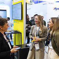 Drei Frauen unterhalten sich auf einem Messestand.