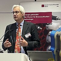 Prof. Dr. Thomas Heimer, Hochschule RheinMain steht vor einem Rednerpult bei der 10 Jahresveranstaltung des Clusters Brennstoffzelle BW