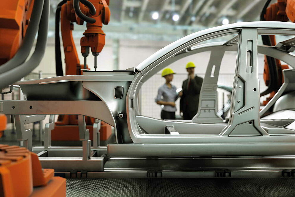 Moderne Automobilproduktionslinie mit Roboterarmen und zwei Personen im Hintergrund