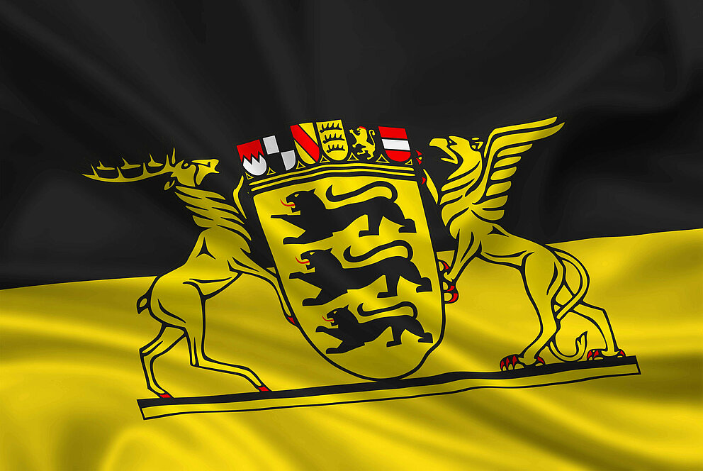 Flagge von Baden-Württemberg mit schwarzem und gelbem Hintergrund. Zwei schwarze Hirsche stehen seitlich und halten gemeinsam ein Wappen zwischen sich. Im Wappen sind drei schwarze Löwen übereinander angeordnet.