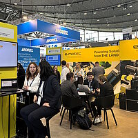 Mehrere Personen tauschen sich auf einem Messestand im Stehen und Sitzen aus.