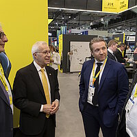 4 Männer im Gespräch, im Hintergrund ist ein Messestand zu sehen