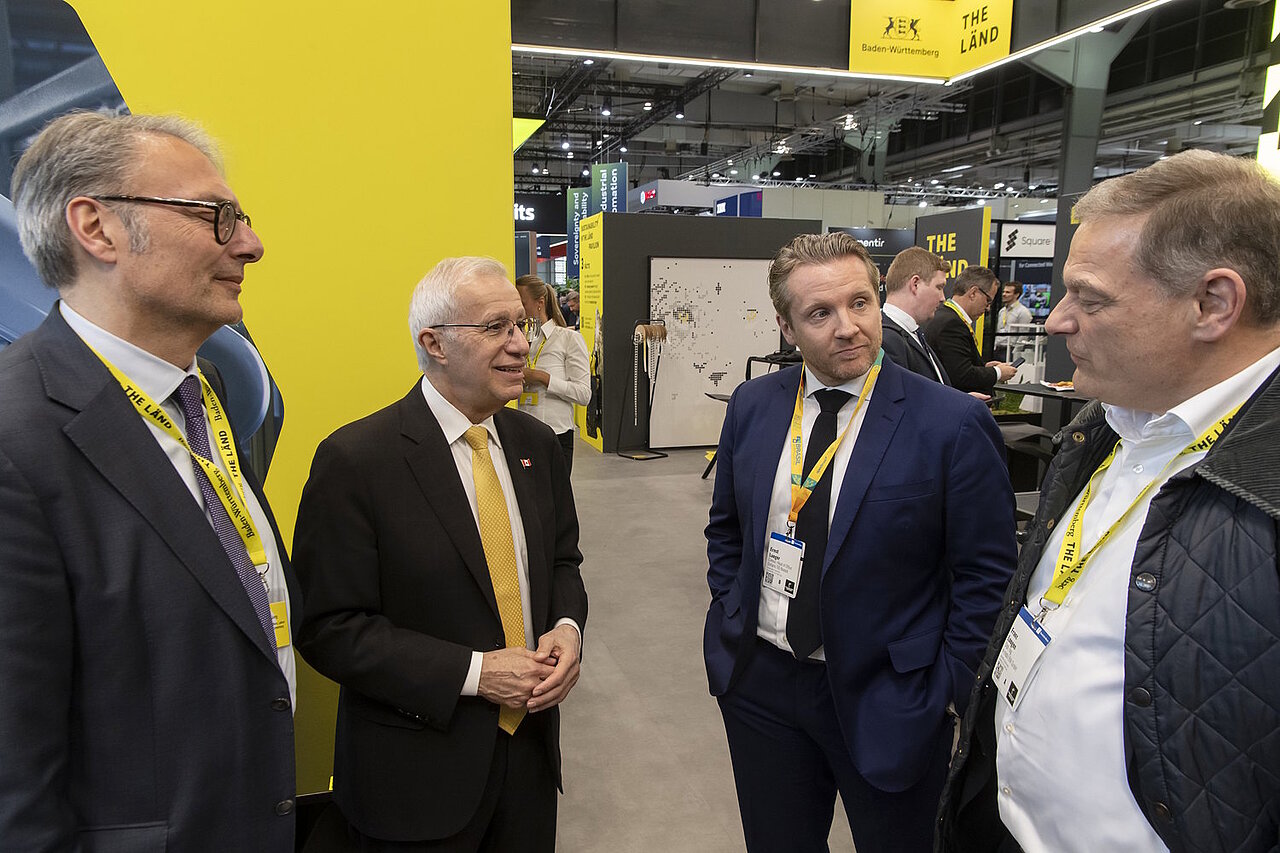 4 Männer im Gespräch, im Hintergrund ist ein Messestand zu sehen