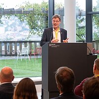 Christoph Erdmenger vom Verkehrsministerium Baden-Württemberg steht bei einer Veranstaltung auf einem Podium und spricht zum Publikum.