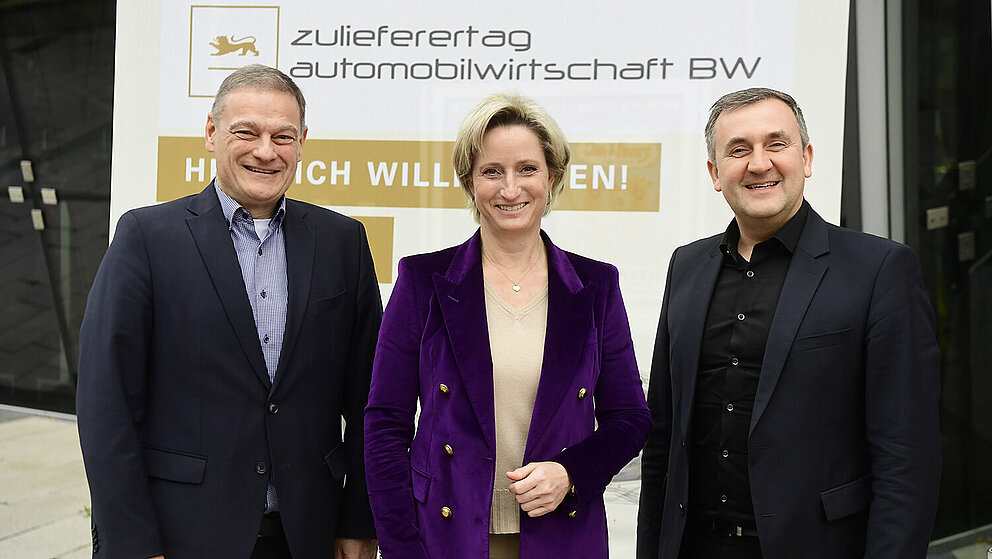 Drei Personen posieren vor dem Zulieferertags-Banner.