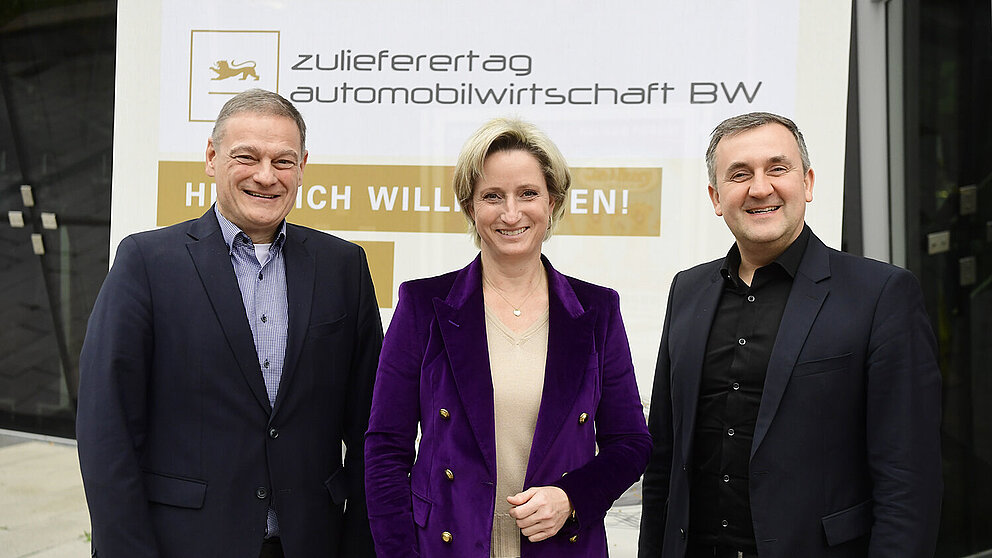 Drei Personen posieren vor dem Zulieferertags-Banner.