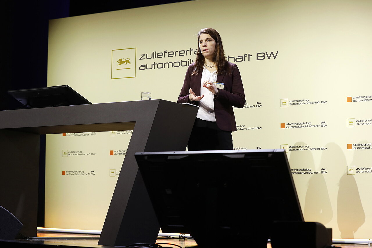 Dr. Anne Piegsa, Prozessmanagerin für Elektromobilität der Business Region Göteborg, spricht auf dem Zulieferertag Automobilwirtschaft BW 2022, sie steht vor einem Rednerpult und hat die Hände gehoben.