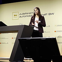 Dr. Anne Piegsa, Prozessmanagerin für Elektromobilität der Business Region Göteborg, spricht auf dem Zulieferertag Automobilwirtschaft BW 2022, sie steht vor einem Rednerpult und hat die Hände gehoben.