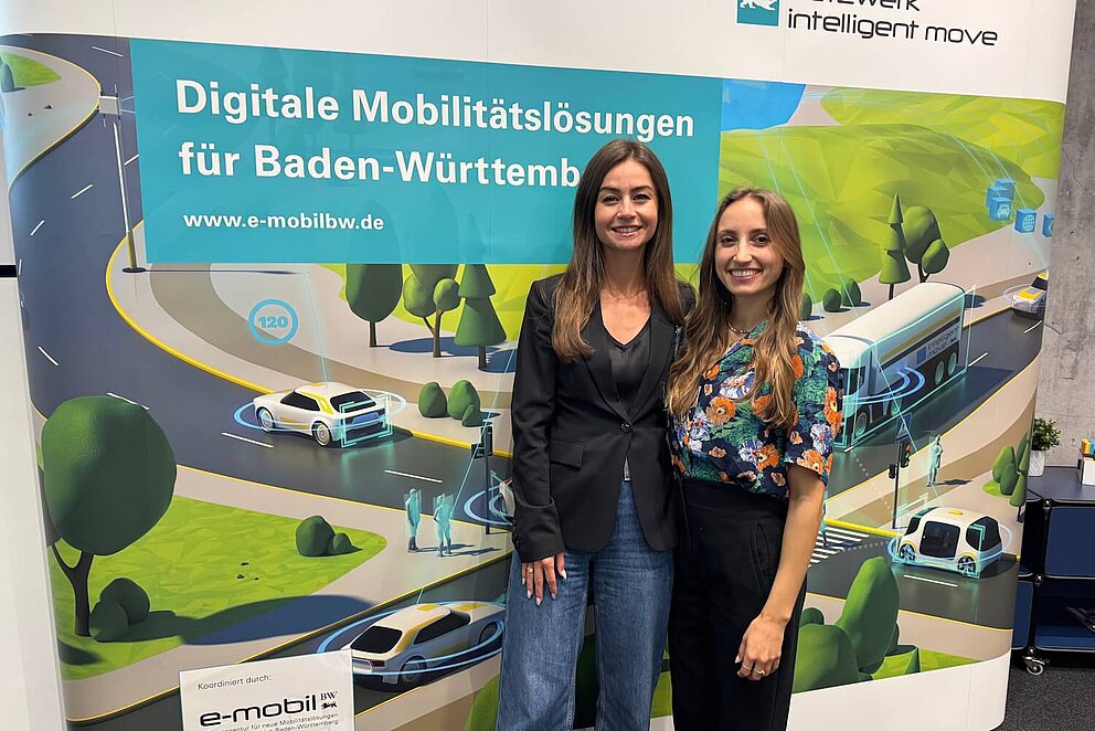 Zwei Mitarbeiterinnen von e-mobil BW vor einer Messewand.