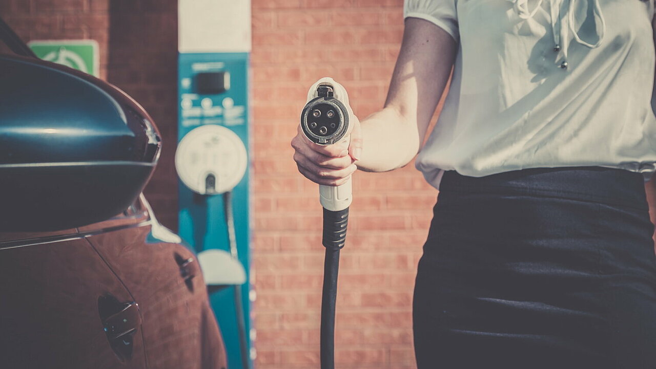 Ein Frau hält ein Ladekabel vor einem E-Auto.