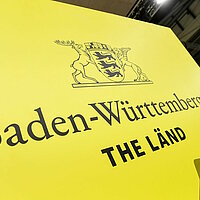 Das Logo von Baden-Württemberg mit dem Slogan "THE LÄND" auf einer Wand des Messestandes von Baden-Württemberg.
