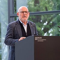Verkehrsminister Winfried Hermann eröffnete das dritte Netzwerktreffen. Er steht auf einem Podium und spricht zum Publikum.