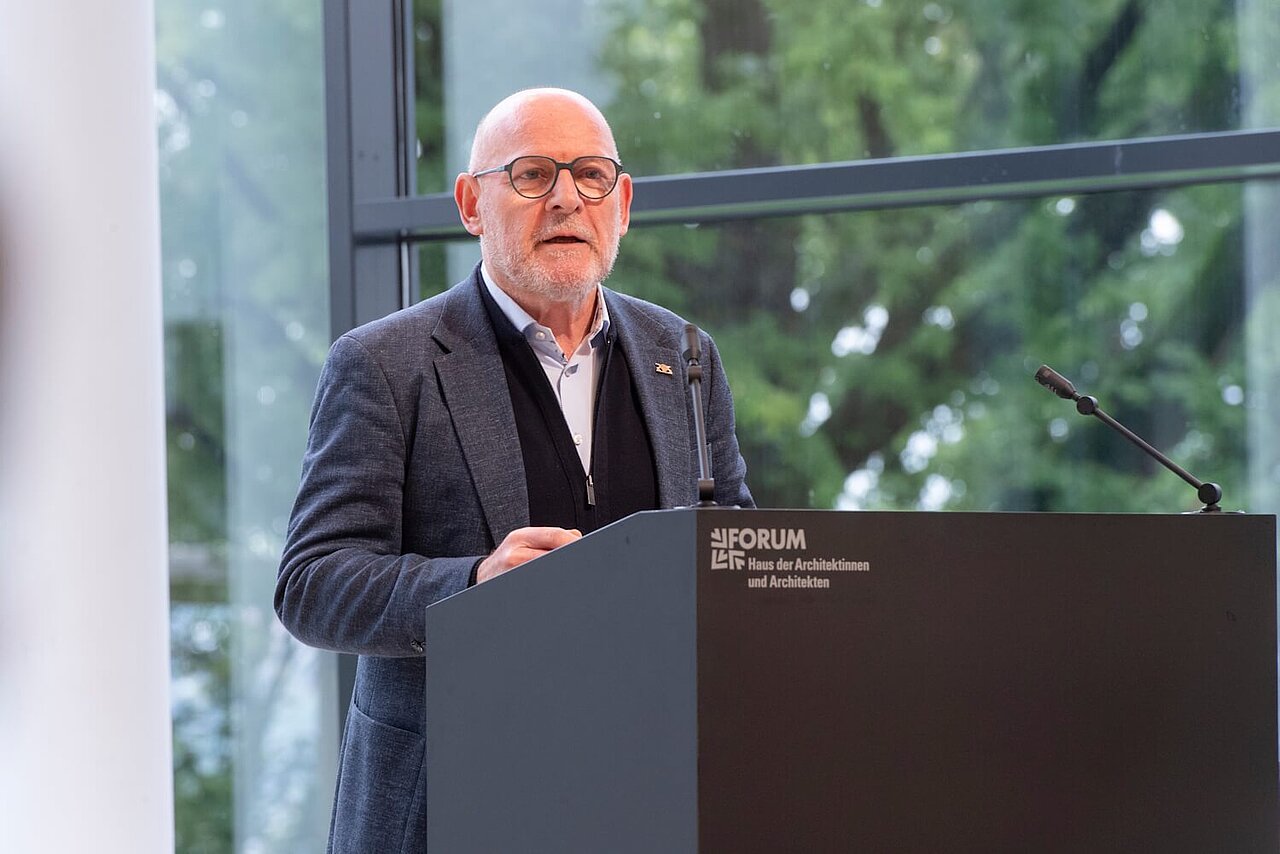 Verkehrsminister Winfried Hermann eröffnete das dritte Netzwerktreffen. Er steht auf einem Podium und spricht zum Publikum.