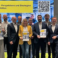 Ein Gruppenfoto aller Beteiligten auf der Bühne, drei Personen halten die vorgestellte Studie "Servicemarkt 2040: Perspektiven und Strategien für freie Kfz-Werkstätten" in die Kamera.