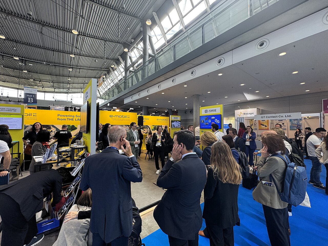 Eine Gruppe Personen informiert sich auf einem Messestand und hört über Kopfhörer einer Führung zu.
