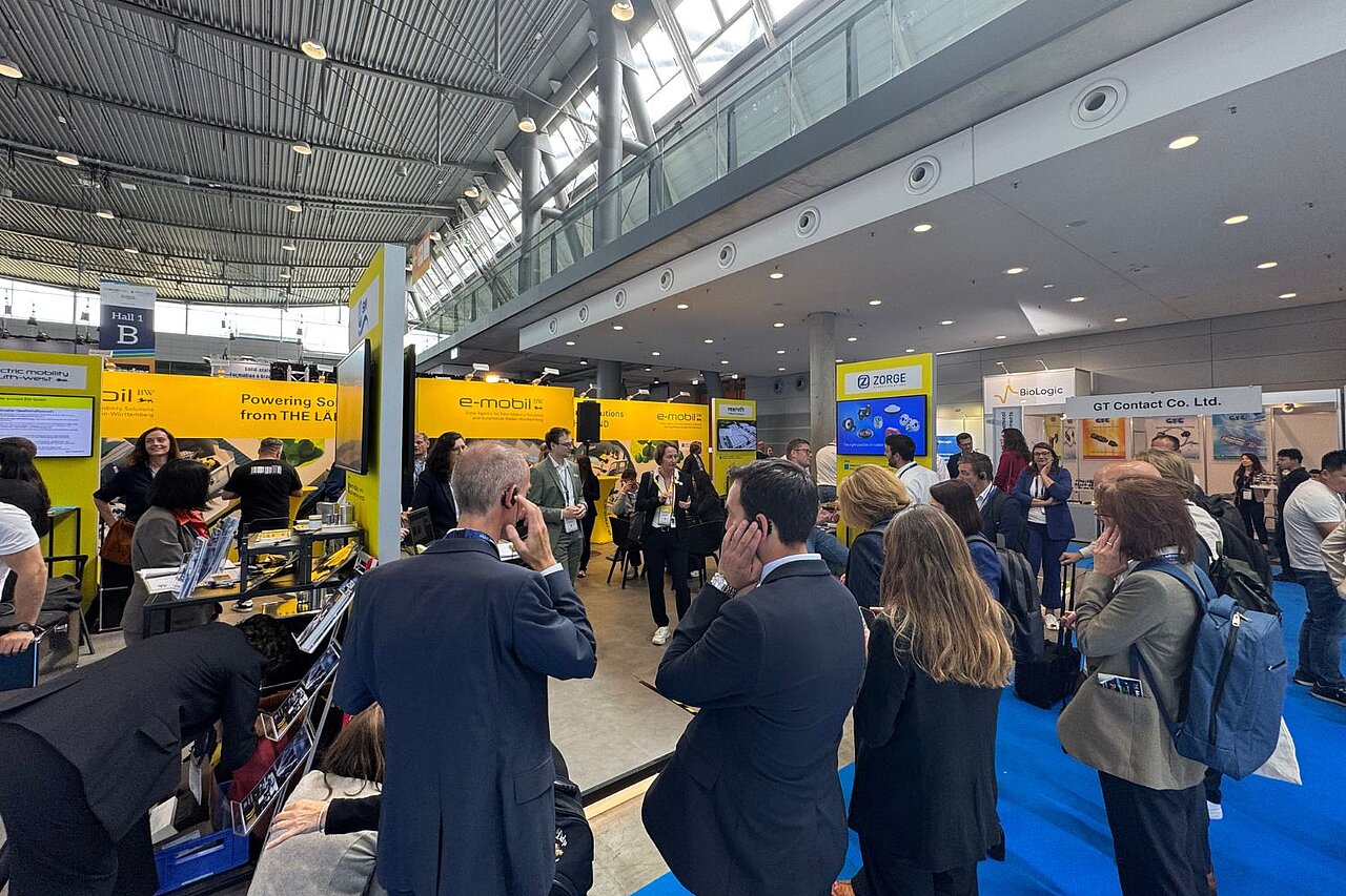 Eine Gruppe Personen informiert sich auf einem Messestand und hört über Kopfhörer einer Führung zu.