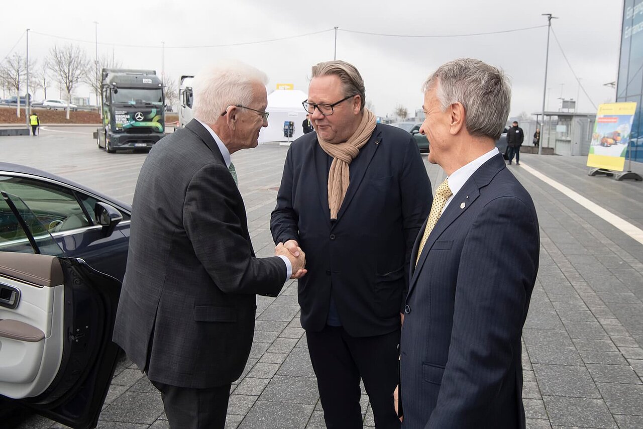 Der Ministerpräsident Winfried Kretschmann bei einer Begrüßung mit zwei weiteren Personen. 