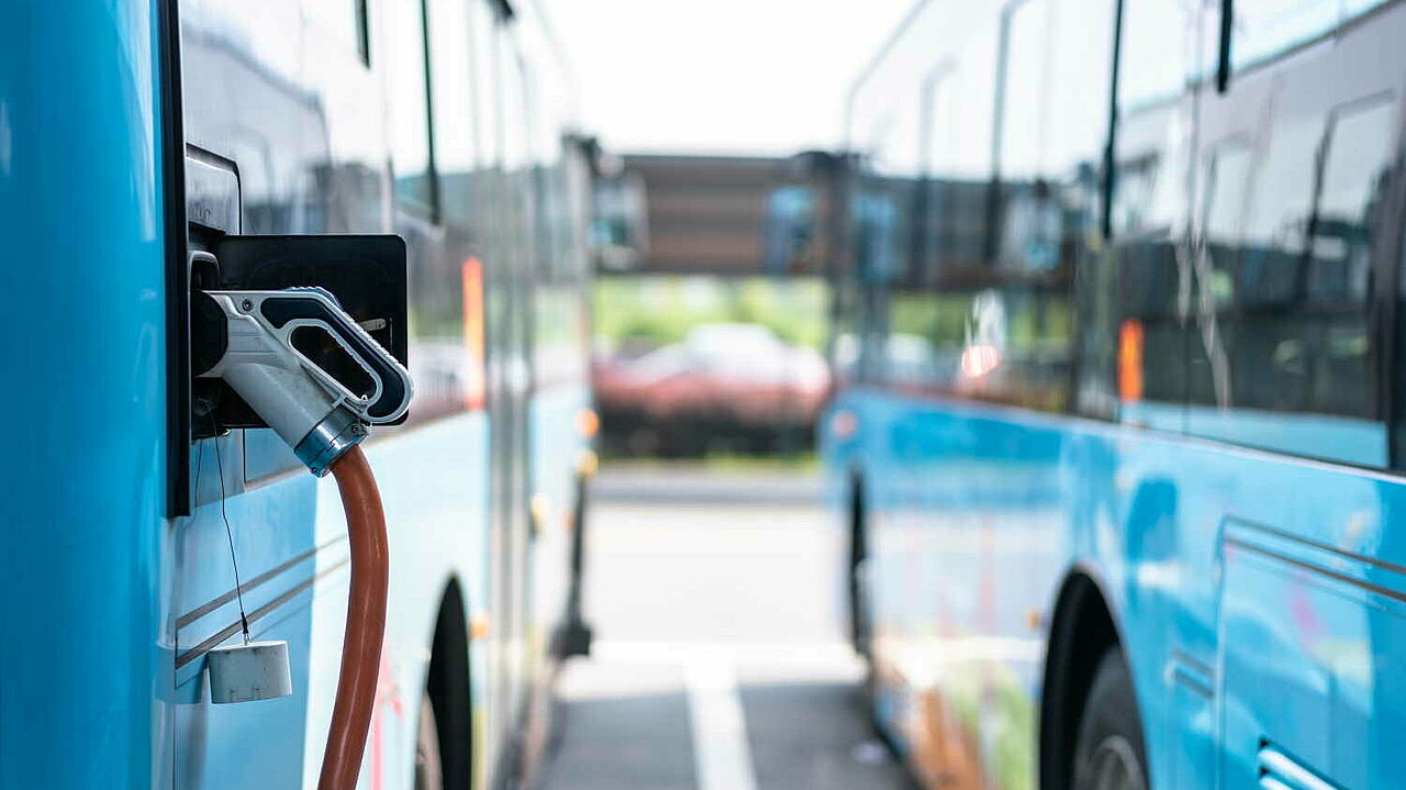 Zwei nebeneinanderstehende E-Busse beim Stromladen auf einem Parkplatz.