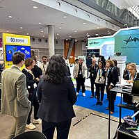 Eine Gruppe Personen informiert sich auf einem Messestand und hört über Kopfhörer einer Führung zu.