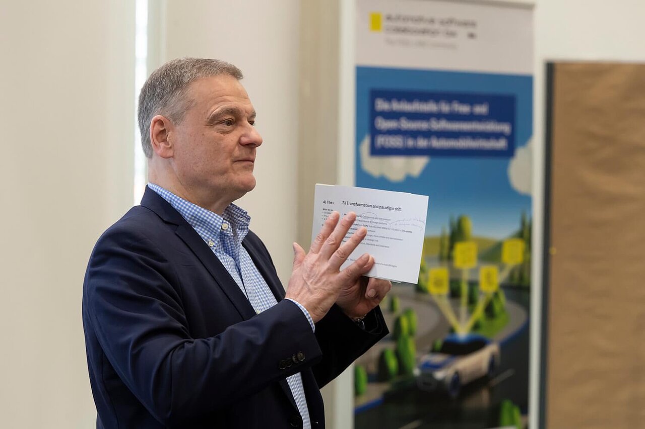 Seitliches Foto von Franz Loogen, der zum Publikum spricht. In der Hand hält er eine Moderationskarte.
