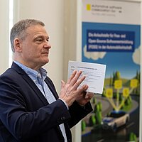 Seitliches Foto von Franz Loogen, der zum Publikum spricht. In der Hand hält er eine Moderationskarte.